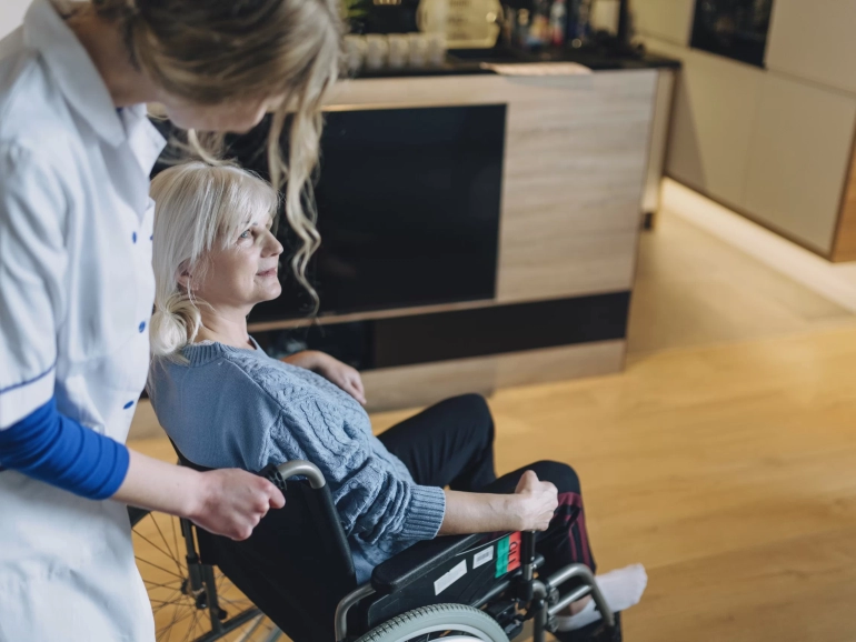 donna anziana in carrozzina assistita da un'infermiera